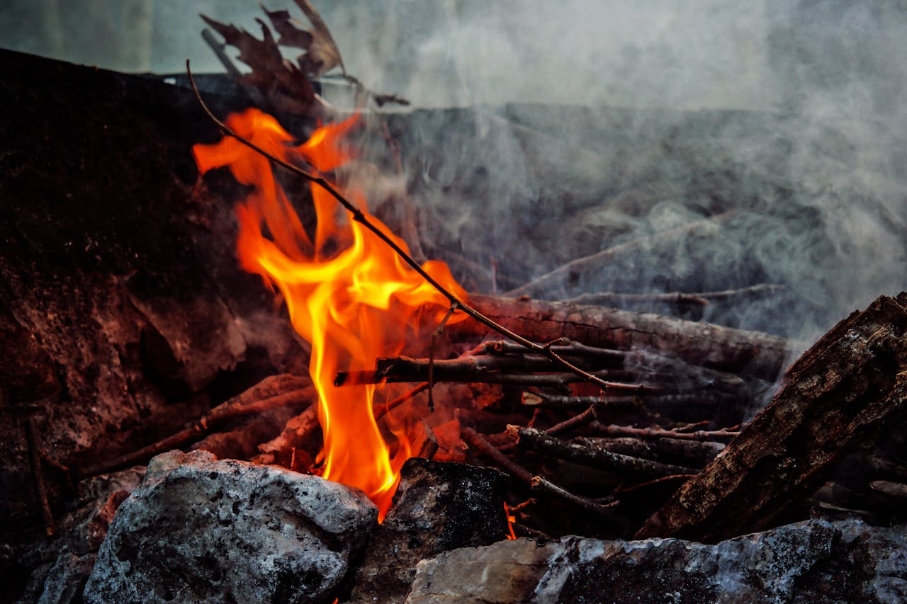 services-03 A close-up shot of a campfire with dancing flames and smoke surrounded by logs and stones.
